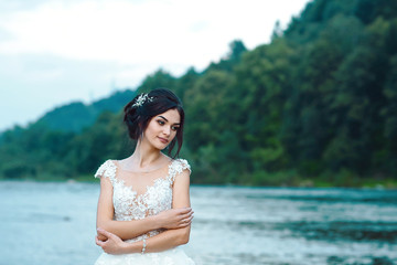 Beautiful bride outdoors in a forest after the sunset against the background of a blue evening near blue lake