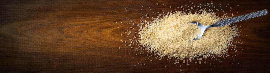 Raw cane sugar. Brown sugar with spoon on wood background. Top view, space for text. Zucchero di canna.