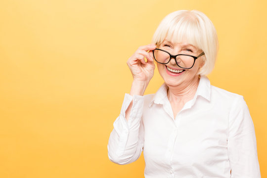 Joyful senior lady in glasses laughing isolated over yellow background. Friendly, mature white haired woman wearing glasses with a smile.