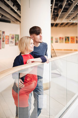 Pregnant wife and husband spend time together in art gallery