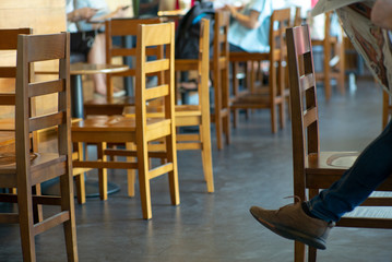Fototapeta na wymiar Selective focus on vintage wooden chairs with person reading the newspaper in the coffee shop