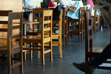 Selective focus on vintage wooden furniture with person reading the newspaper in the coffee shop with crowd of people working in background
