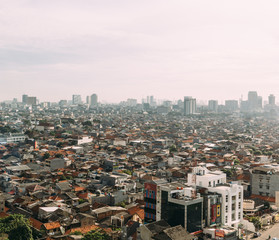 Fototapeta premium Central Jakarta Cityscape with high rise, skyscrapers and red tile hip roof local buildings with fog in the morning.