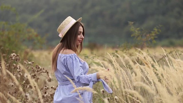 Pregnant woman in nature try on knitted hat. Background of field and white fance near the farm. mountains