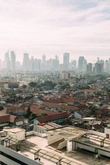 Fototapeta na wymiar Jakarta Cityscape with high rise, skyscrapers and red tile hip roof local buildings with fog in the morning.