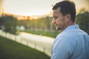 .Portrait of handsome middle-aged man in sunmmer morning park. Pensive calm man in casual clothes...