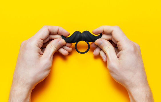Men's hands hold Black mustache, props for photo booths, carnival, parties on yellow background top view flat lay copy space Father's day Creative party decoration concept