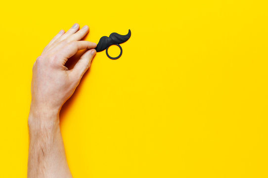 Men's hands hold Black mustache, props for photo booths, carnival, parties on yellow background top view flat lay copy space Father's day Creative party decoration concept