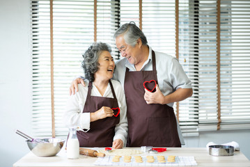 senior couple holding red cookies cutters in heart shape.