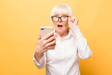 Wow! Phone conversation. Surprised aged woman using phone, isolated over yellow background. - obrazy, fototapety, plakaty