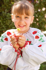 Cute young girl in an embroidered shirt against green bushes background. The girl looks a little funny because her milk teeth fell off and adults have not yet grown up