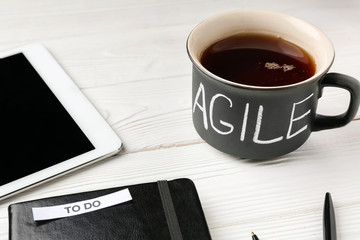 Cup of coffee with word AGILE on wooden background