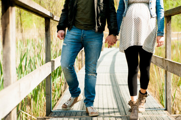 young expecting couple, dressed in modern casual way, walking on wooden pier during sunny day in...