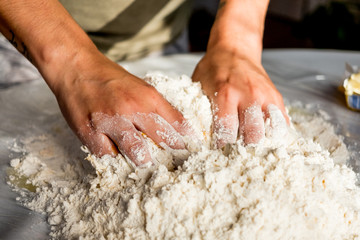 close up of young italian woman woman hands making fresh homemade italian pasta on table with flour