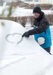 Mann zeichnet Herz auf die Schneebedecket Windschutzscheibe, Love