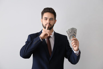 Businessman with bribe showing silence gesture against light background. Concept of corruption