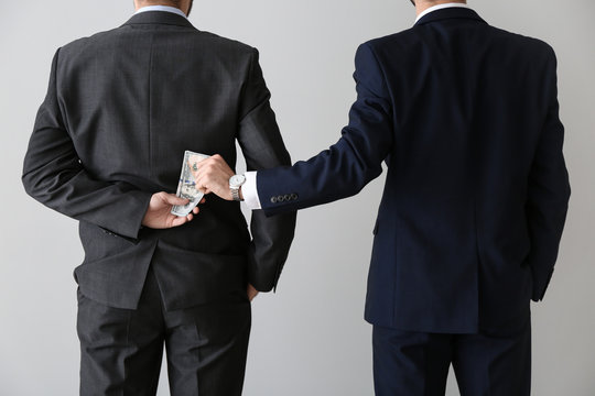 Businessman taking bribe from man on light background. Concept of corruption