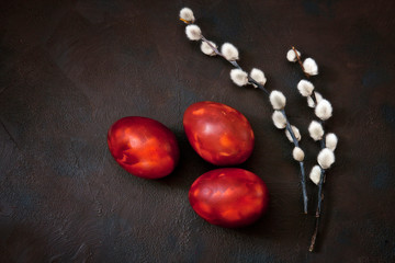 Easter decoration – three colored eggs and pussy willow. Close up, top view, flat lay on dark concrete background