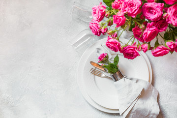 Romantic table setting with pink roses as decor, dishware, silverware, and decorations. Top view.
