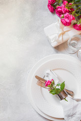 Romantic table setting with pink roses as decor, dishware, silverware, and decorations. Top view.