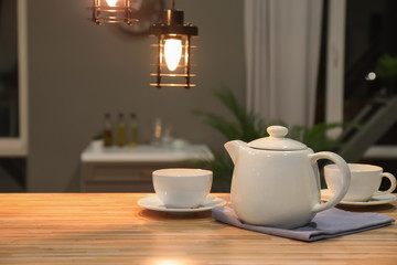 Teapot with cups on wooden table in kitchen