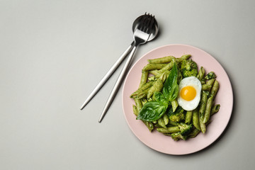 Plate with tasty pesto pasta and fried egg on grey background