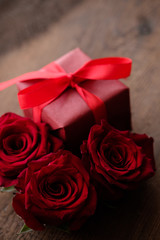 A gift in craft paper with a red ribbon and with roses nearby on a wooden table. Close up