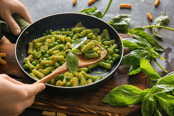 Woman cooking tasty pesto pasta in pan