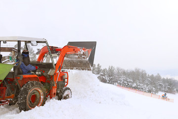 The tractor pours snow with his bucket on the ski slope. The work of the snowcat in the winter time. Preparation of the sports ground for competitions. Snow drifts and mechanization in working with