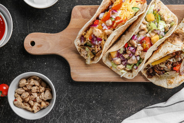 Wooden board with tasty tacos on dark table