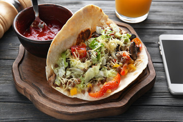 Board with tasty taco and sauce on wooden table