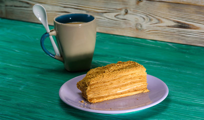 A piece of cake and a cup of coffee on a green wooden background.