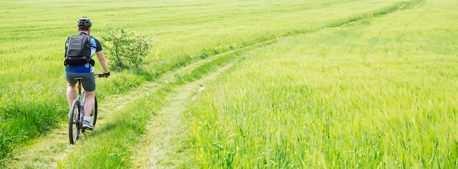 Poster man riding bicycle by trail in green barley field. copy space. w © phpetrunina14