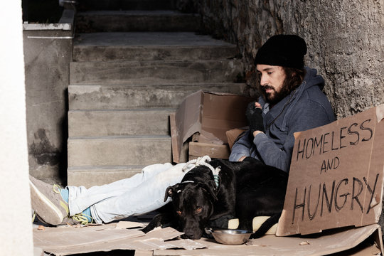 Houseless man sitting with his dog on backstreet