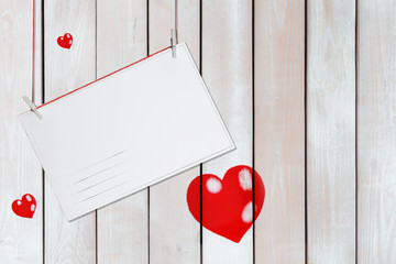 greeting paper card and three red hearts on wooden white background with copy space