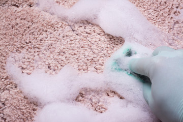 Spring cleaning in house. Hand in green glove cleaning carpet by chemical liquid carpet shampoo...