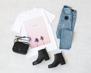 White t-shirt with pink print, blue jeans, small black cross body bag and leather ankle boots on...