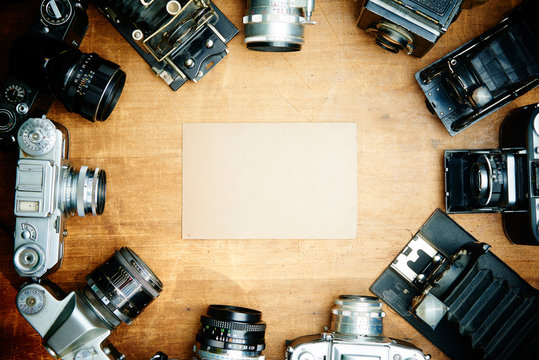 Collection of old vintage cemaras around blank frame on wooden table. Selective focus