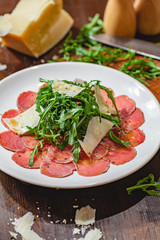 Meat carpaccio with arugula and parmesan cheese on white plate. Close up