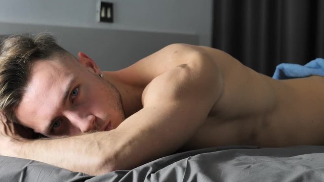 Totally naked sexy young man with muscular body on bed looking away