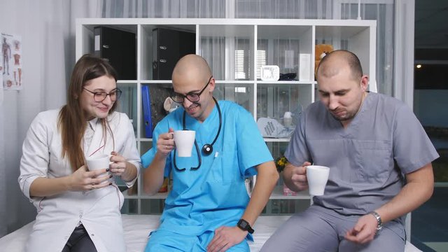 Three doctors in the staffroom talk and drink coffee at the break.