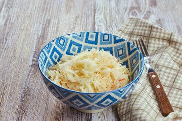 salad of pickled cabbage. Traditional Russian appetizer sauerkraut with carrots in a plate on a white wooden table. Rustic style. Selective focus and copy space, close-up.
