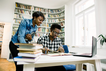 Male and female african students studying together for finals. Happy young university students studying with laptop in college library sitting together at table with books and laptop.