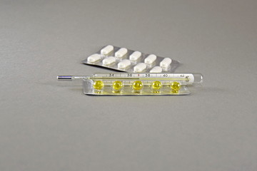 Tablets and mercury thermometer on grey background, close up