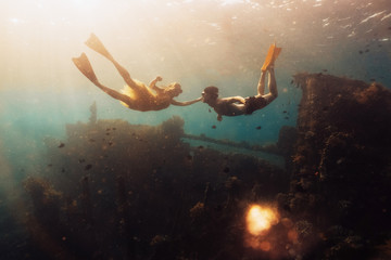 Young couple snorkeling together in a blue tropical sea. sunken ship in background