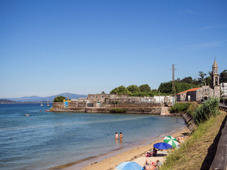 Turistas tomando el sol en la Ensenada Pobla de Caramiñal en La Coruña, con el campanario al fondo en el verano de 2018