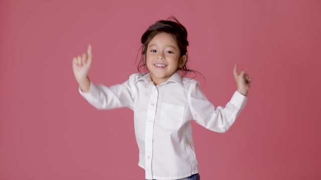little child girl in white shirt dancing on pink background.