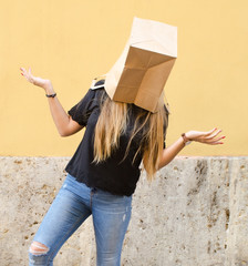 Young woman wearing a paper bag over her head in front of yellow background