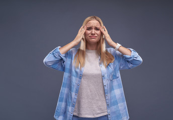 Unhappy young lady in blue shirt touching temples