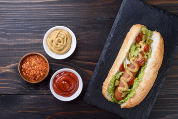 Tasty hot dog with  mustard and  ketchup on wooden background, top view